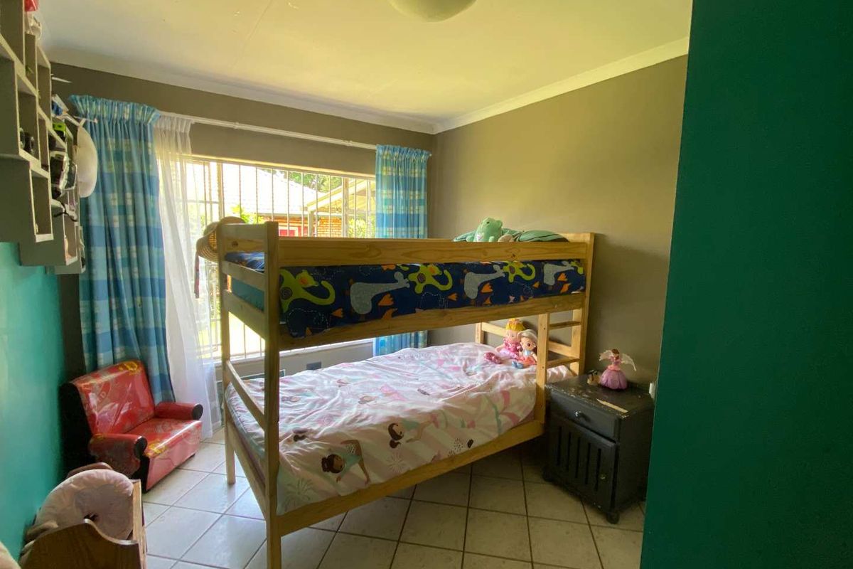 A bedroom featuring tiled flooring, a large window with security bars, and a ceiling-mounted light fixture.