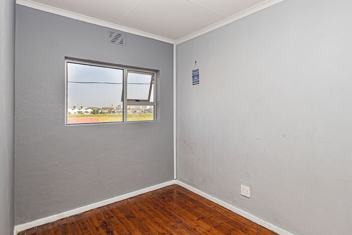 An empty bedroom featuring timber flooring, grey painted walls, and an aluminium window frame with exterior views.
