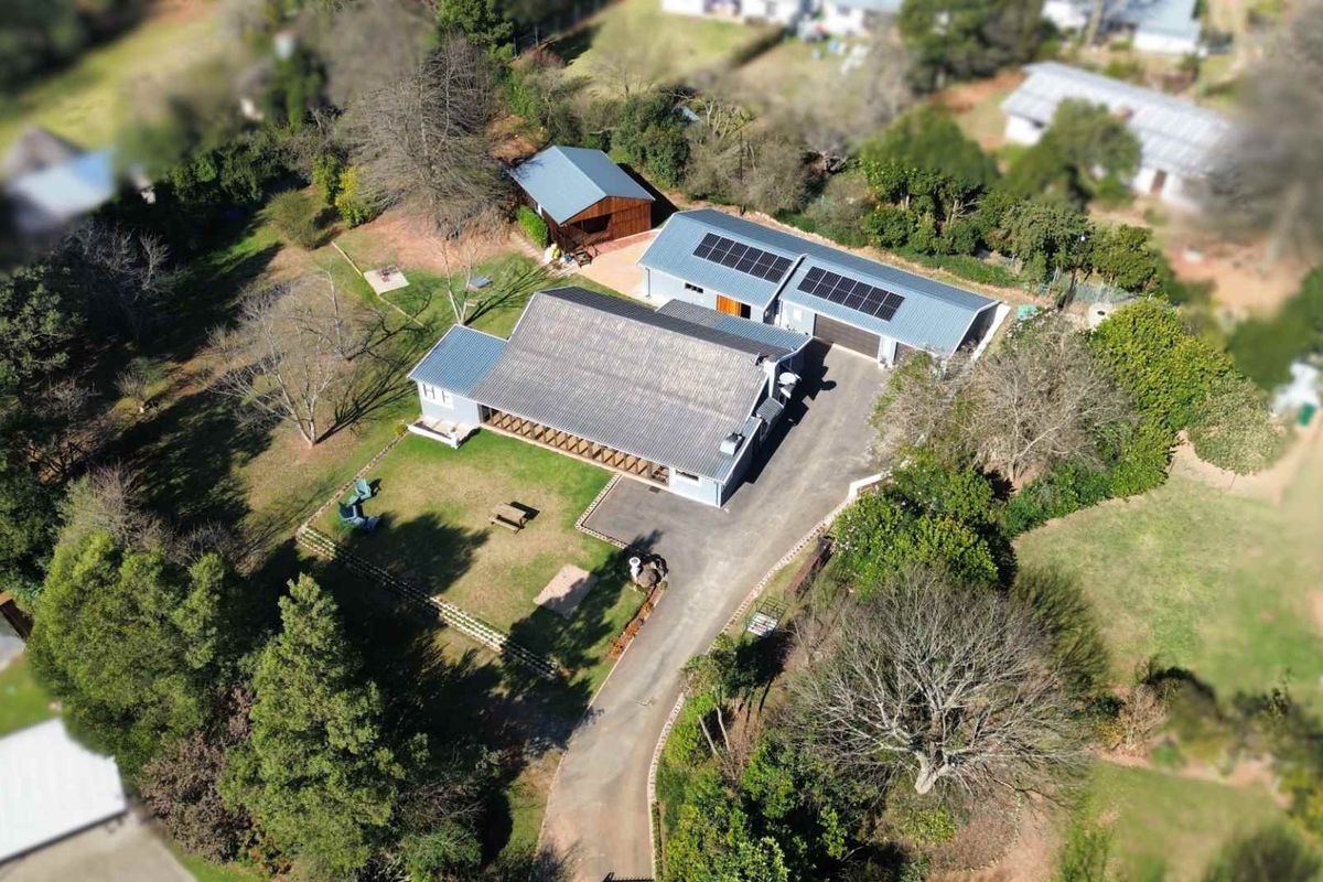 Aerial view of the property featuring a main residence, detached garage, and expansive garden grounds with solar panel installation on the roof.