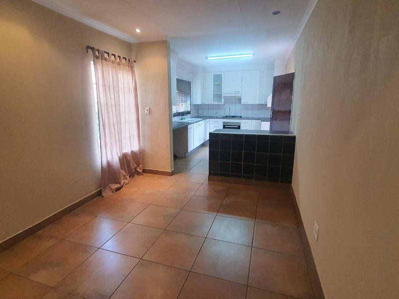 Open plan living and kitchen area featuring tiled flooring, a tiled breakfast counter, and built-in kitchen cabinetry with integrated appliances.