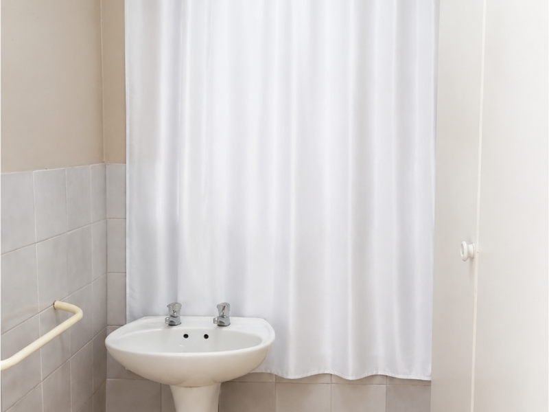 A functional bathroom featuring a pedestal basin, tiled splashback, and a safety grab rail, providing a clean and practical space.