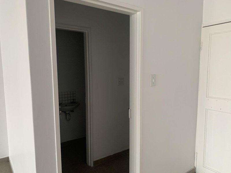 A view through a doorway into a small, empty bathroom featuring a wall-mounted basin with a tiled splashback.