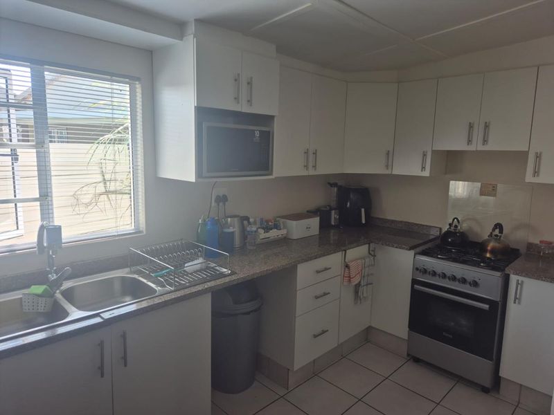A functional kitchen featuring white cabinetry, granite countertops, a stainless steel sink, and a freestanding gas stove with a built-in microwave.