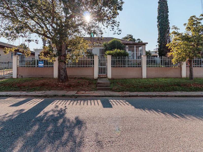 Front elevation of a residential property featuring a perimeter wall with metal security fencing, a pedestrian gate, and a driveway entrance.