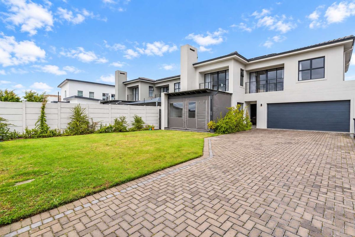 Rear view of a modern double-story home featuring a paved driveway, manicured lawn, enclosed patio area, and a double garage.