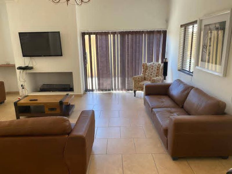 A living room featuring tiled flooring, a built-in fireplace, and large sliding glass doors with vertical blinds providing access to the exterior.