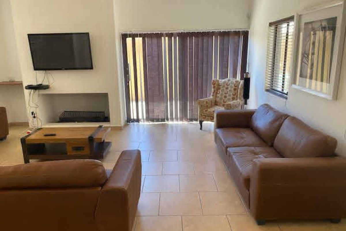 A living room featuring tiled flooring, a built-in fireplace, and large sliding glass doors with vertical blinds providing access to the exterior.