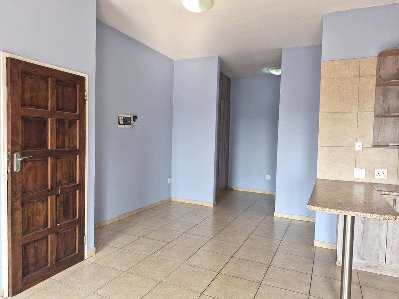 An open-plan living and kitchen area featuring tiled flooring, a breakfast counter, and built-in cabinetry, presenting a clean and functional space.