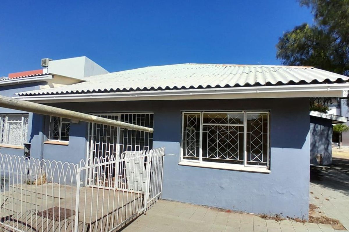 Rear exterior view of the property featuring a corrugated metal roof, paved patio area, and security bars on windows and sliding doors.