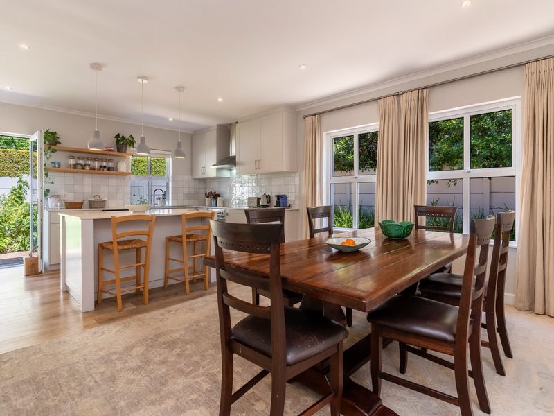 Bright open-plan kitchen and dining area featuring a central island, modern cabinetry, and direct access to the garden through glass doors.