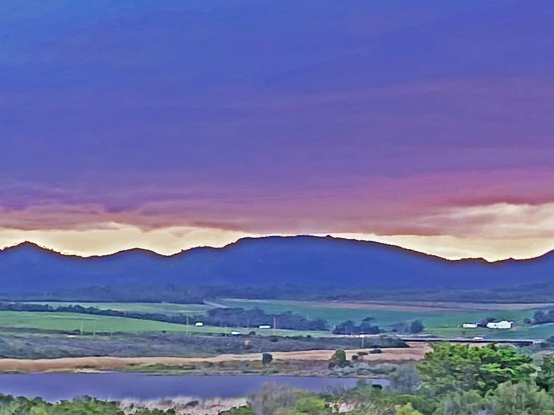 A scenic landscape view featuring rolling hills, a body of water, and a vibrant sunset sky over the residential land.