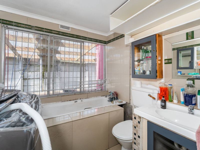 A dated bathroom featuring a built-in bathtub, vanity cabinet, and ceramic wall tiling, requiring cosmetic updates to modernize the space.