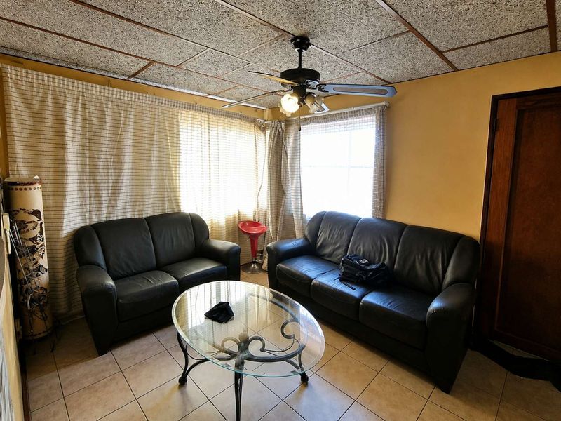 A living room featuring tiled flooring, a ceiling fan, and textured ceiling tiles, offering a dated aesthetic ready for modernization.