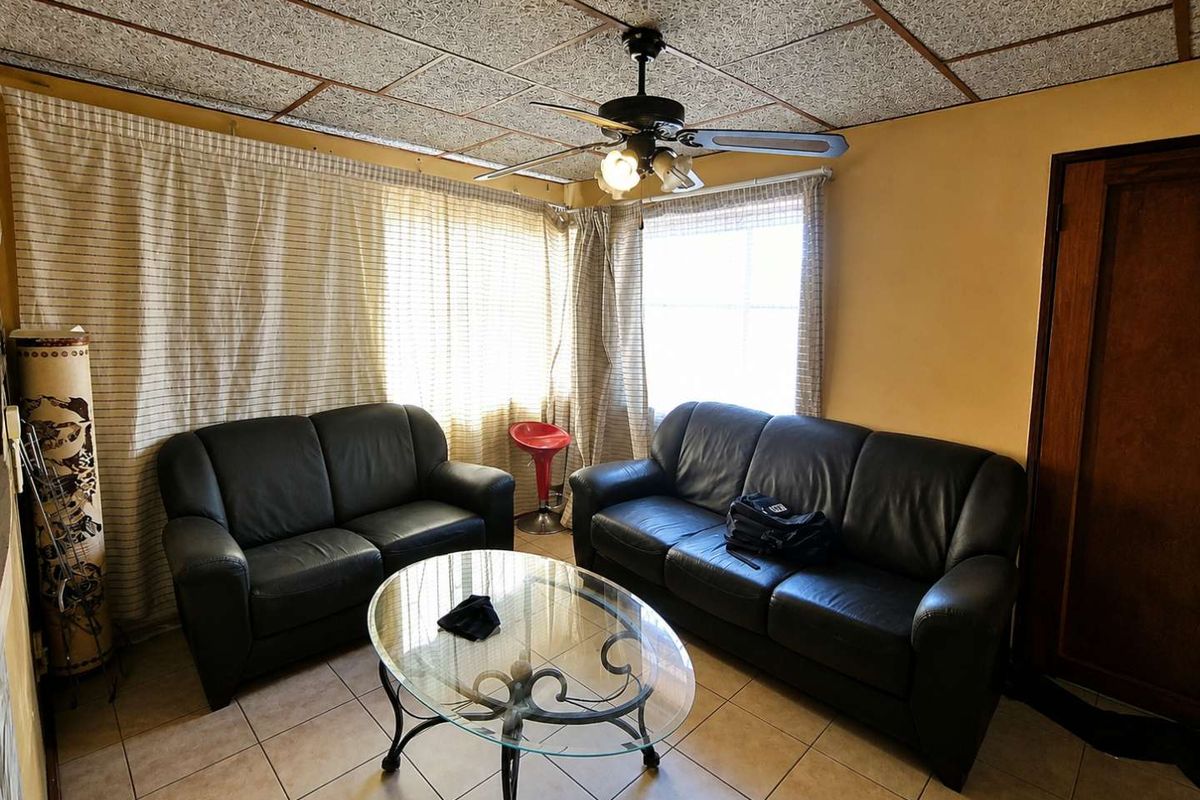 A living room featuring tiled flooring, a ceiling fan, and textured ceiling tiles, offering a dated aesthetic ready for modernization.
