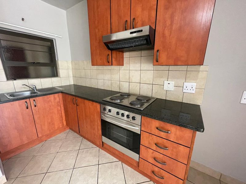 A functional kitchen featuring wooden cabinetry, granite countertops, a built-in oven with electric hob, and a tiled backsplash.