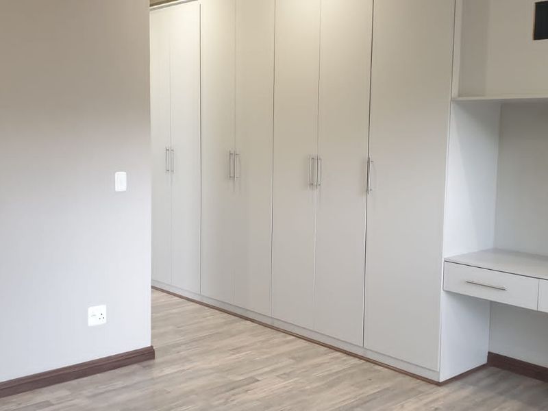 A bright, empty bedroom featuring extensive built-in cupboards and a integrated desk area with modern laminate flooring.