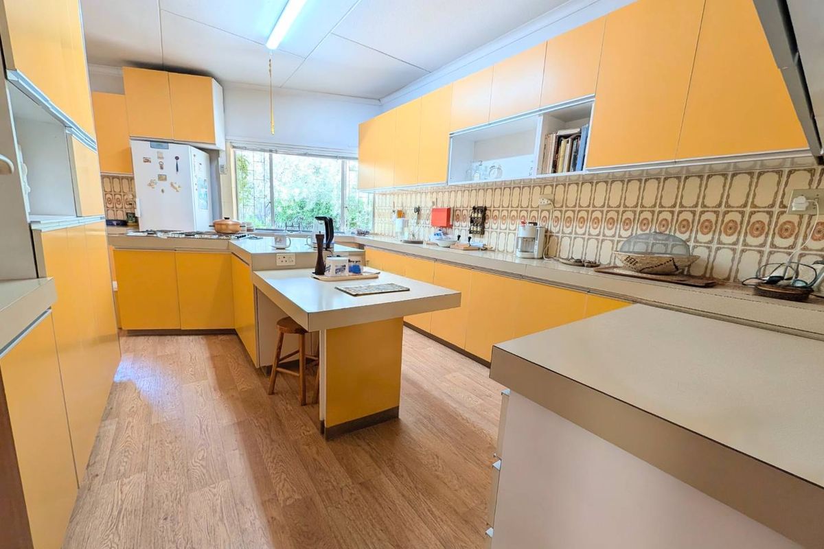 A spacious kitchen featuring bright yellow cabinetry, a central island, wood-look flooring, and large windows providing natural light.