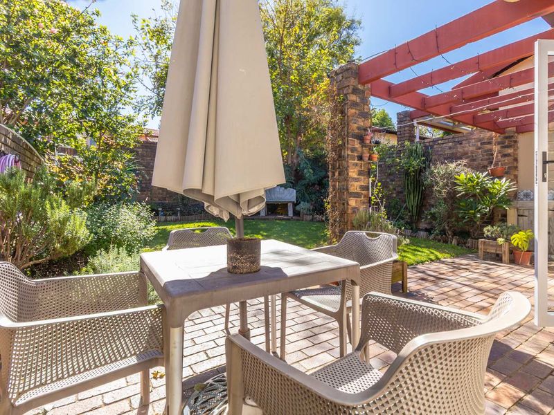A private rear garden featuring a paved patio area with a timber pergola, brick boundary walls, and established greenery.