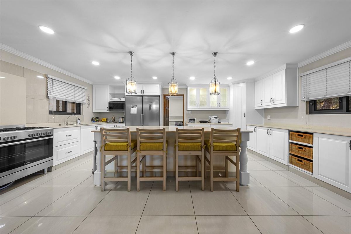 Spacious modern kitchen featuring white cabinetry, a large central island with breakfast seating, tiled flooring, and integrated stainless steel appliances.