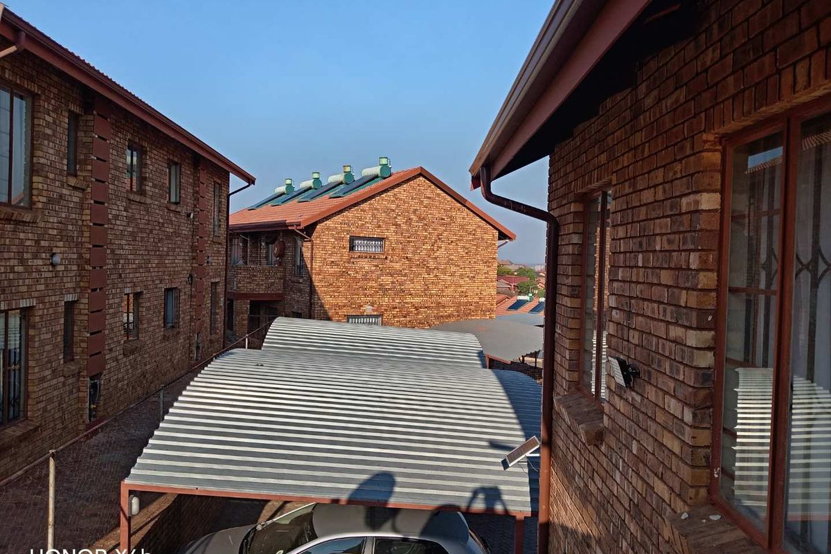 Exterior view of a face brick apartment complex featuring a corrugated metal carport and solar water heating installations on the roof.
