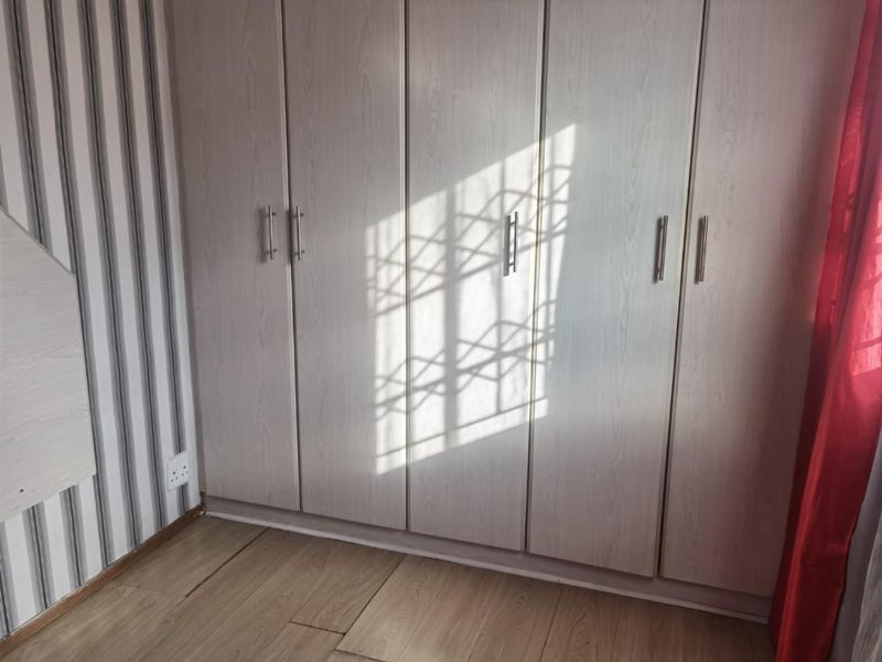 A bedroom featuring light-toned built-in cupboards, laminate flooring, and decorative wallpaper.