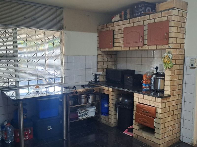 A functional kitchen featuring brick-built cabinetry, granite countertops, a built-in stove, and tiled backsplash, offering a rustic aesthetic with potential for modernization.
