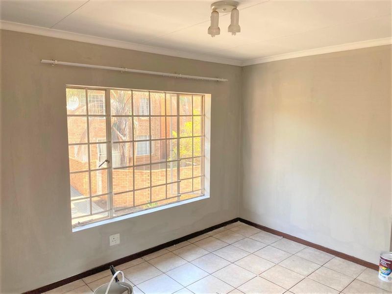 An empty bedroom featuring tiled flooring, a large window with security bars, and neutral wall finishes, ready for personalization.