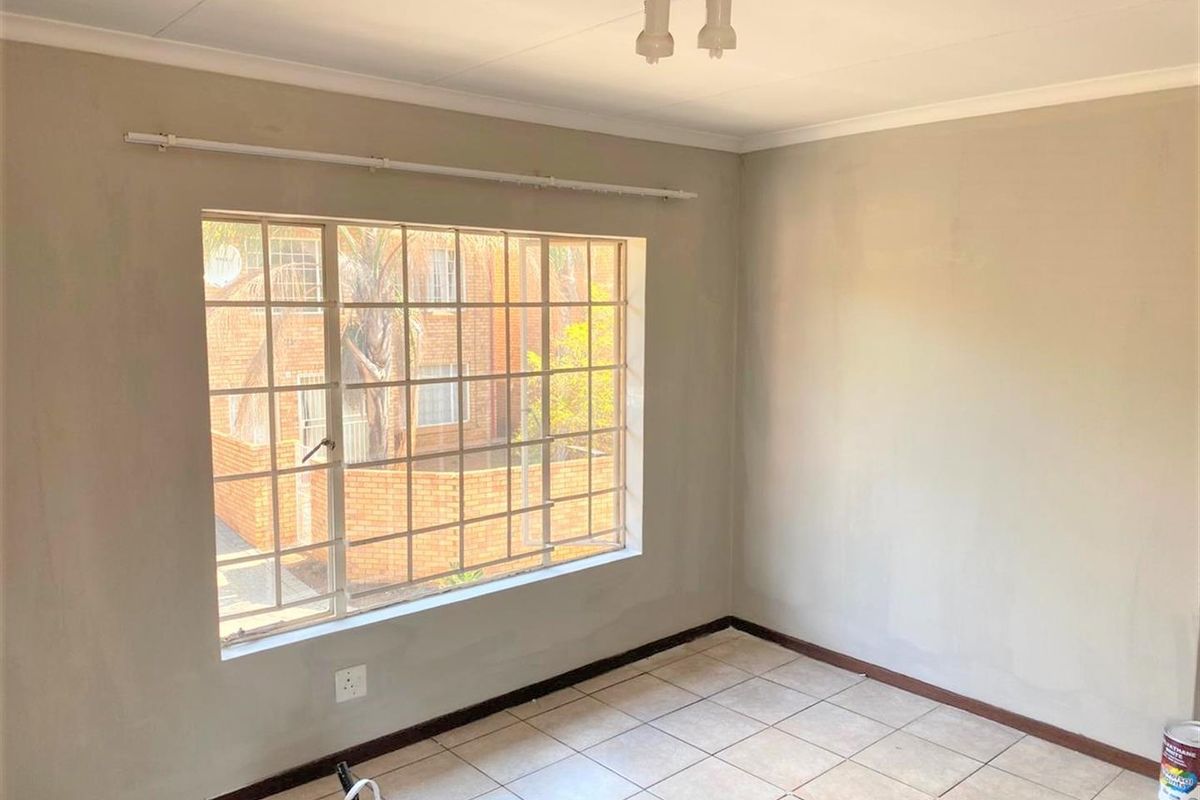 An empty bedroom featuring tiled flooring, a large window with security bars, and neutral wall finishes, ready for personalization.