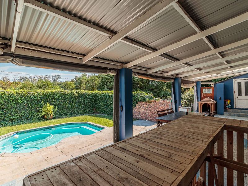 Covered outdoor patio area featuring a built-in bar counter, overlooking a private swimming pool and landscaped garden with a brick retaining wall.