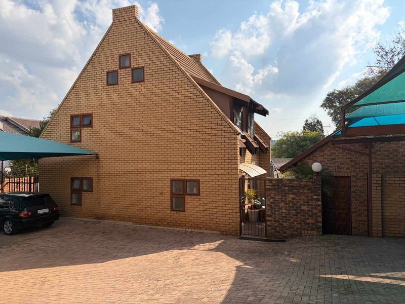 A view of the front exterior of a facebrick cluster home featuring a paved driveway, shade cloth carport, and secure gated entrance.