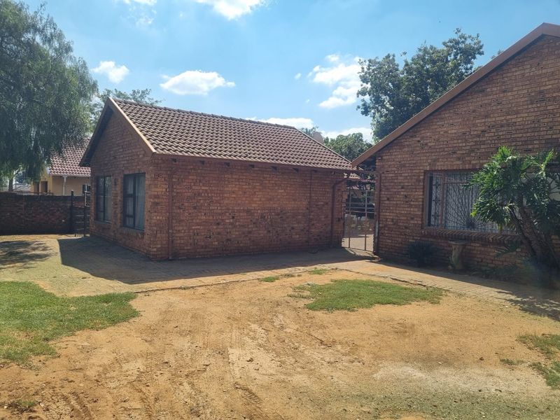 Rear view of the face brick house featuring a tiled roof, paved pathways, and security features on the windows.