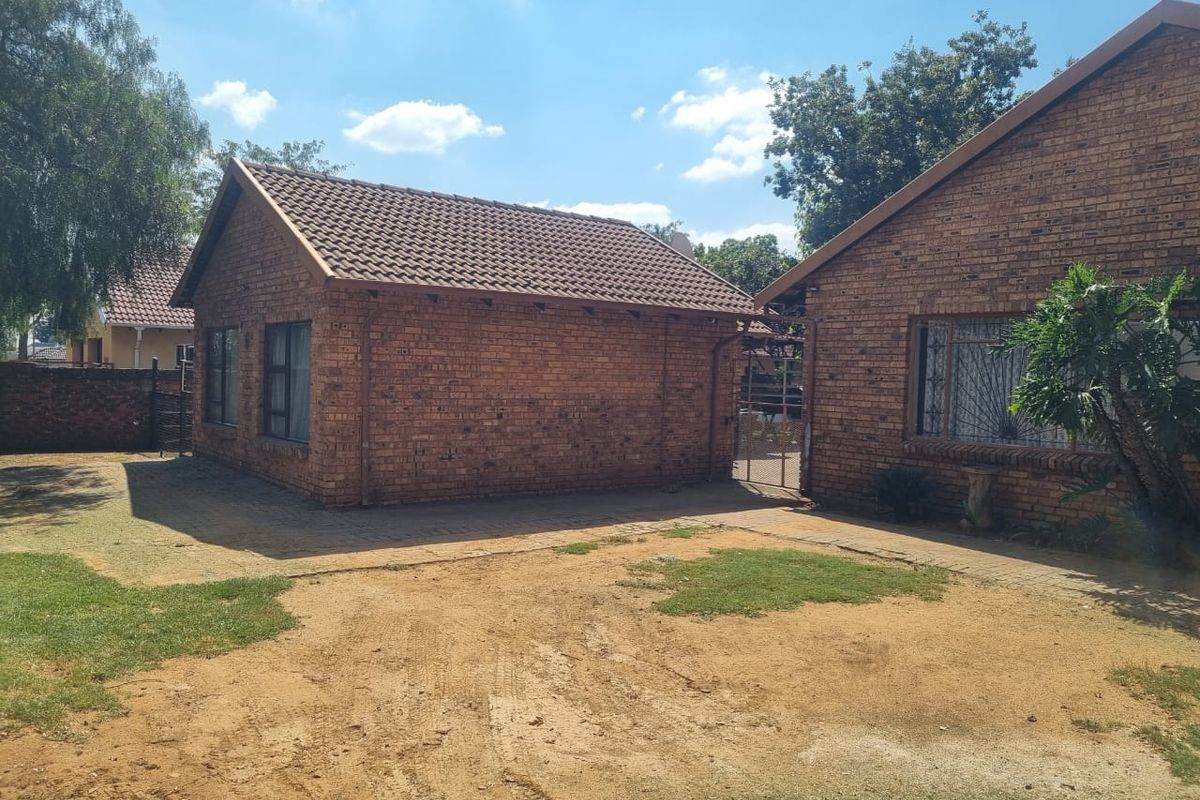 Rear view of the face brick house featuring a tiled roof, paved pathways, and security features on the windows.