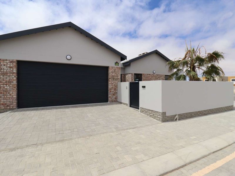 Modern front elevation featuring a double garage, paved driveway, and a secure boundary wall with a pedestrian gate.