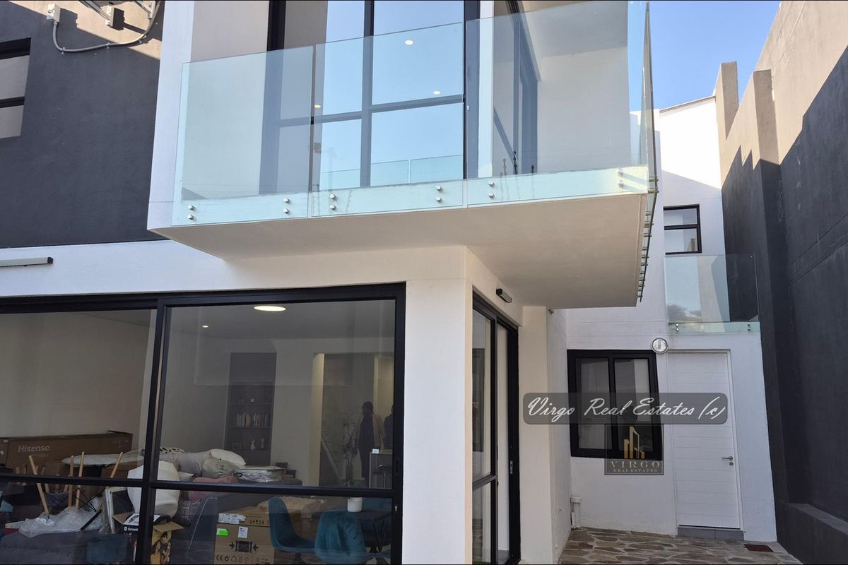 Rear view of a modern townhouse featuring a glass balcony, large aluminium sliding doors, and a paved courtyard area.