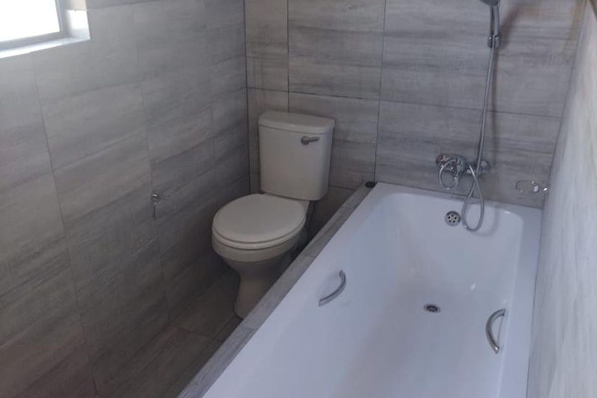 A clean, functional bathroom featuring a built-in bathtub with a shower mixer and a standard toilet, finished with modern grey wall and floor tiles.