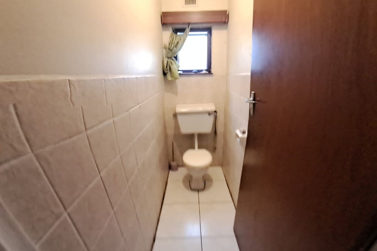 A compact guest toilet featuring neutral wall tiles, white floor tiling, and a standard porcelain toilet suite.