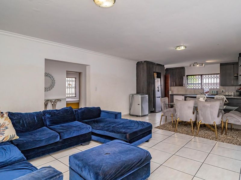 Spacious open-plan living and dining area featuring tiled floors, neutral walls, and a functional kitchen with built-in cabinetry.