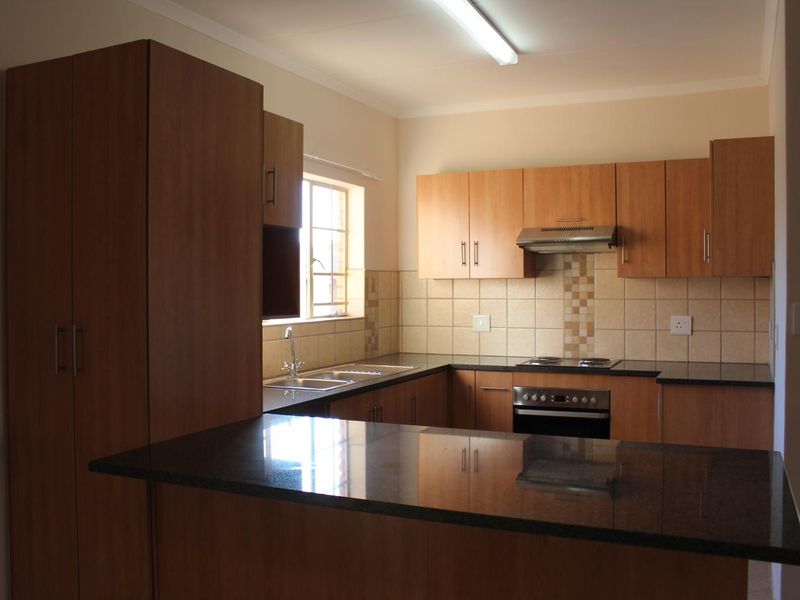 A functional kitchen featuring wood-finish cabinetry, dark granite countertops, a built-in oven, electric hob, and a tiled backsplash.