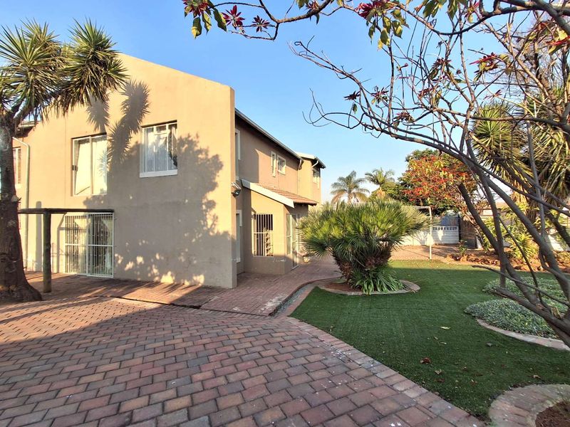 Rear exterior view of the property featuring a paved driveway, artificial lawn area, and secure sliding door access.
