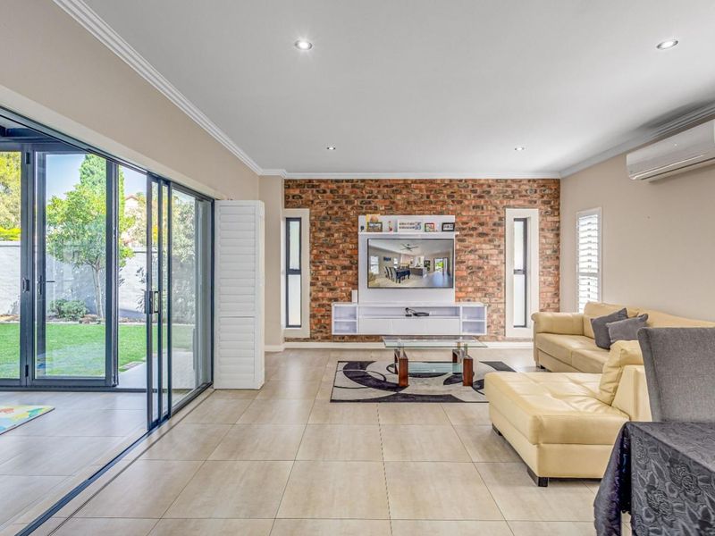 Spacious living room featuring an exposed brick wall, large sliding glass doors opening to the garden, and modern tiled flooring.