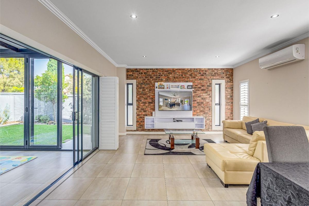 Spacious living room featuring an exposed brick wall, large sliding glass doors opening to the garden, and modern tiled flooring.
