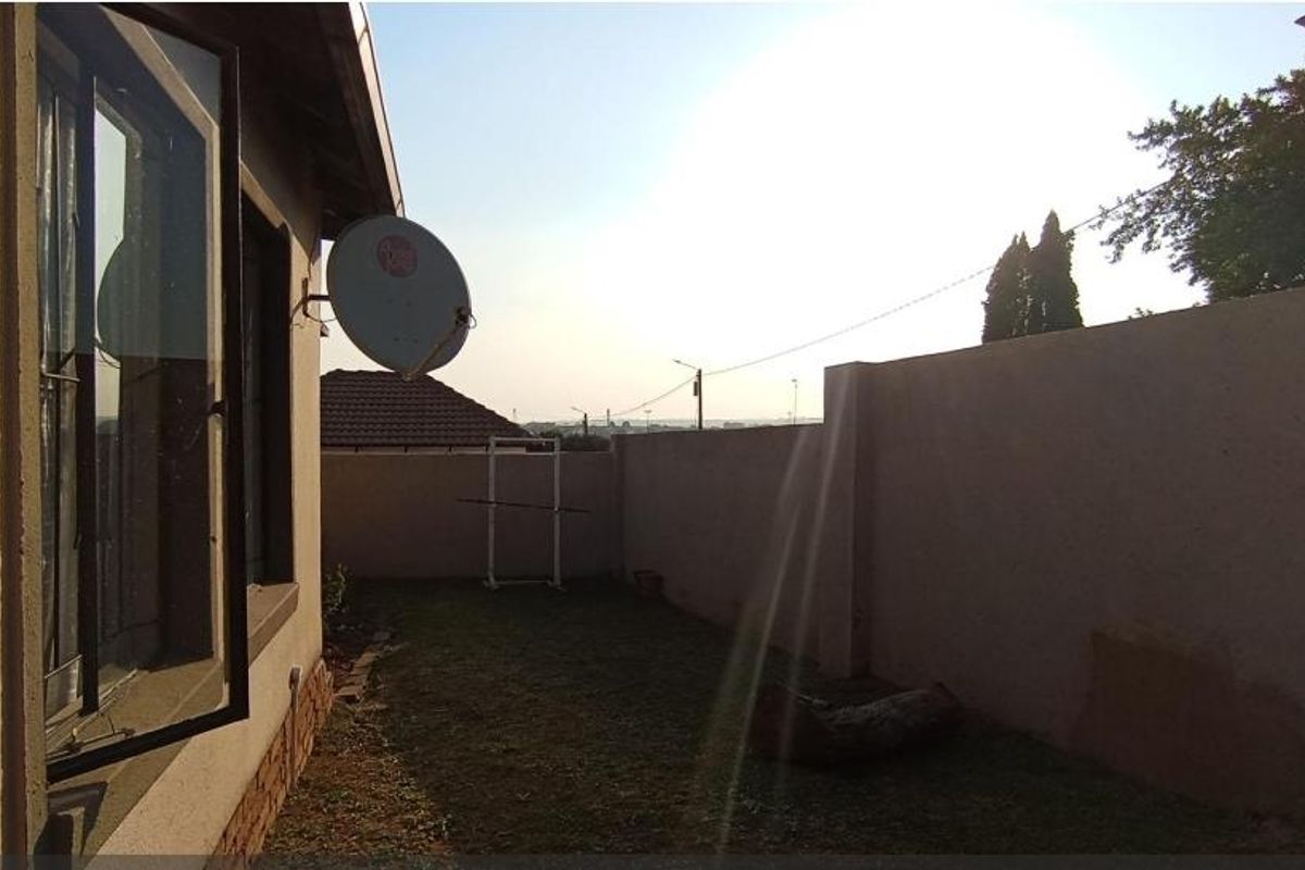 A side exterior view of the property featuring a grass lawn, boundary wall, and satellite dish mounted to the building facade.