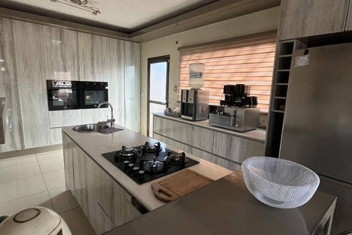 Modern kitchen featuring a central island with a built-in gas hob, integrated double ovens, sleek cabinetry, and a breakfast bar area.