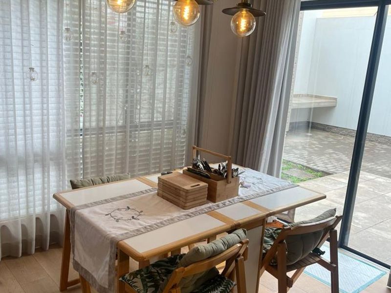 A bright dining area featuring hardwood flooring, modern pendant lighting, and large sliding glass doors providing direct access to an outdoor patio space.