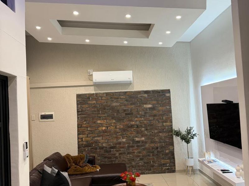 Modern living room featuring a striking exposed brick feature wall, recessed ceiling with integrated downlights, and a sleek floating media console.