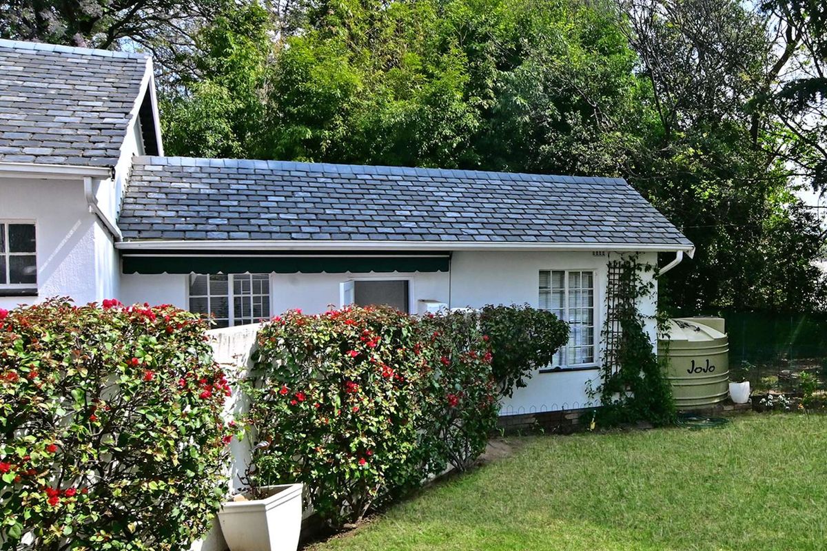 A well-maintained rear exterior view of the house featuring a slate roof, white facade, and a water tank set within a landscaped garden.