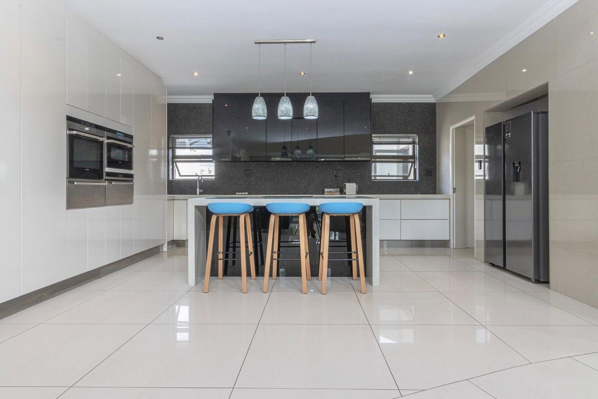 Modern kitchen featuring high-gloss cabinetry, a central island with stone countertops, built-in appliances, and polished tile flooring.