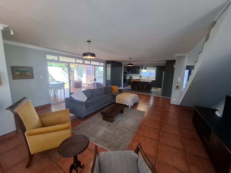 Spacious open-plan living area featuring terracotta floor tiles, a modern kitchen with island, and seamless access to the outdoor patio through sliding glass doors.