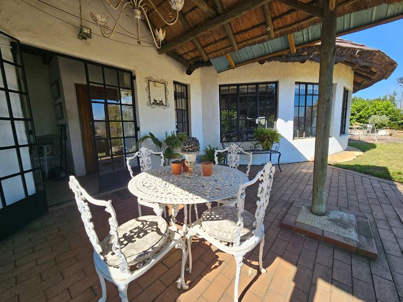 A covered patio area featuring a traditional thatched roof, timber support posts, and brick paving, providing a charming outdoor space for relaxation.