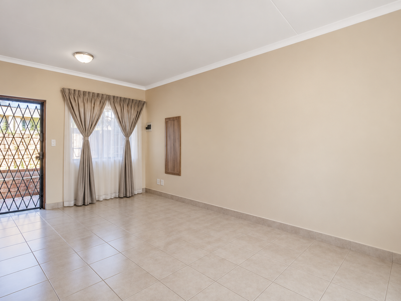 A bright and spacious living area featuring neutral tiled flooring, clean walls, and direct access to an outdoor space through a secure door.